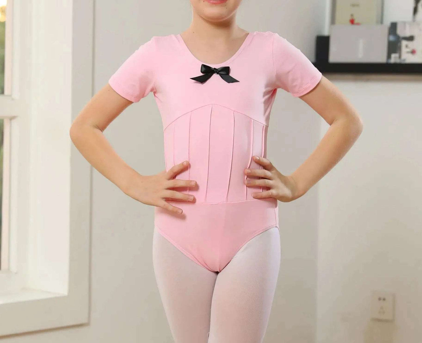front of girl's pink short sleeved ballet leotard with bow on front