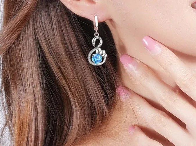 woman wearing silver swan earrings with blue cubic zirconia